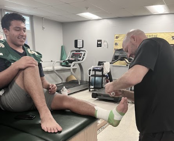 Darrick Linenberger tapes an athletes foot in preparation for an upcoming football game.