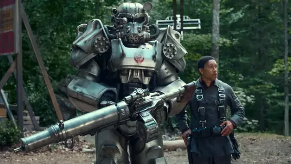 Maximus (Aaron Moten) wears his Brotherhood Squire Fatigues while standing next to a Brotherhood soldier in T-60 Power Armor.