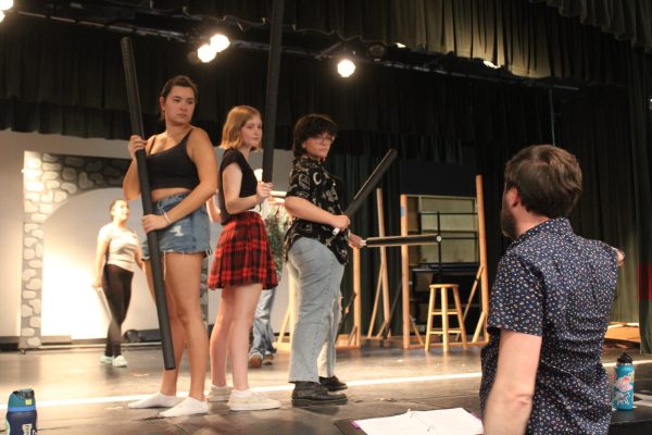 SHHS theatre director Jeremy Cooley, directs cast members Willow Eichen, Jules Booth, and Hailey Westervoorde, on stage blocking.

