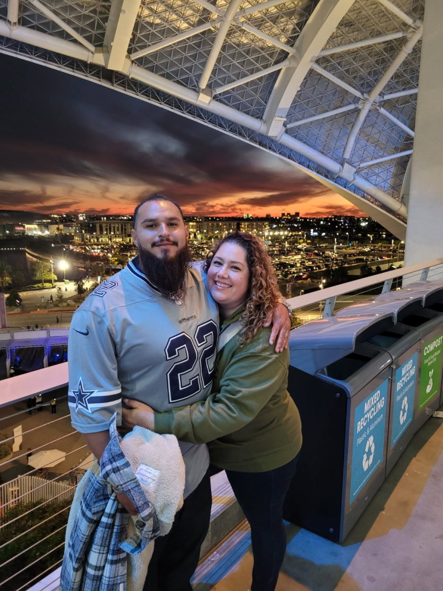Assistant football coach Alex Carrasco poses for a photo with his wife at the SoFi Stadium while wearing Dallas Cowboys gear.

