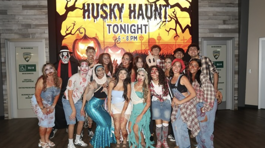 ASB Husky Haunt scare actors pose for a photo in front of the Husky Haunt flyer.